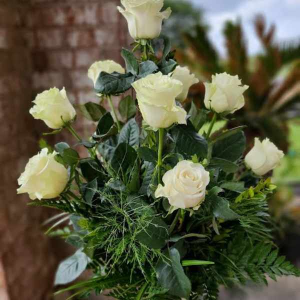 White roses arranged in a tall vase with dense greenery