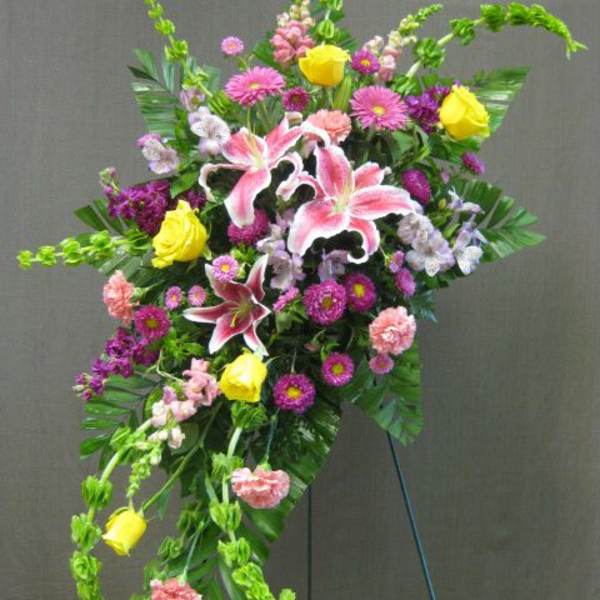 Standing floral spray with pink lilies, yellow roses, and purple blooms