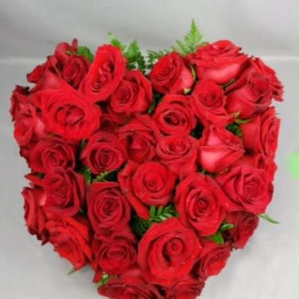 Heart-shaped bouquet of red roses with small green accents