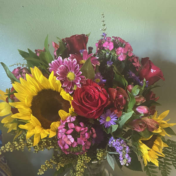 Bouquet of sunflowers, red roses, and pink mixed flowers in a glass vase