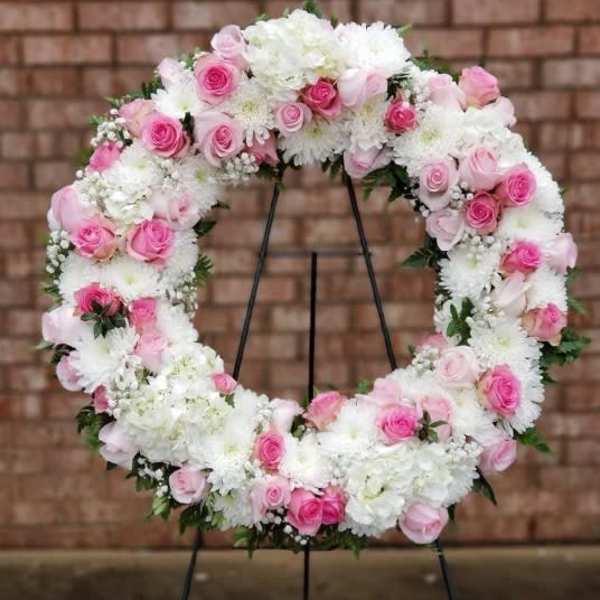 Pink and white floral wreath on a black stand