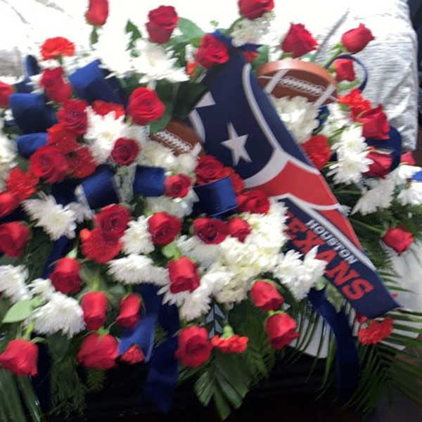 Red and white funeral spray with blue ribbon and Houston Texans logo on a casket