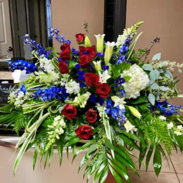 Large red, white, and blue floral spray with roses, lilies, and delphinium in an elongated design
