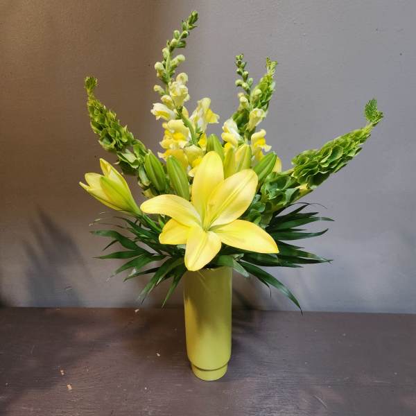 Yellow lilies and snapdragons arranged in a tall vase