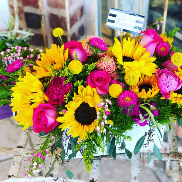 Bright bouquet with sunflowers, pink roses, and magenta flowers in a white container