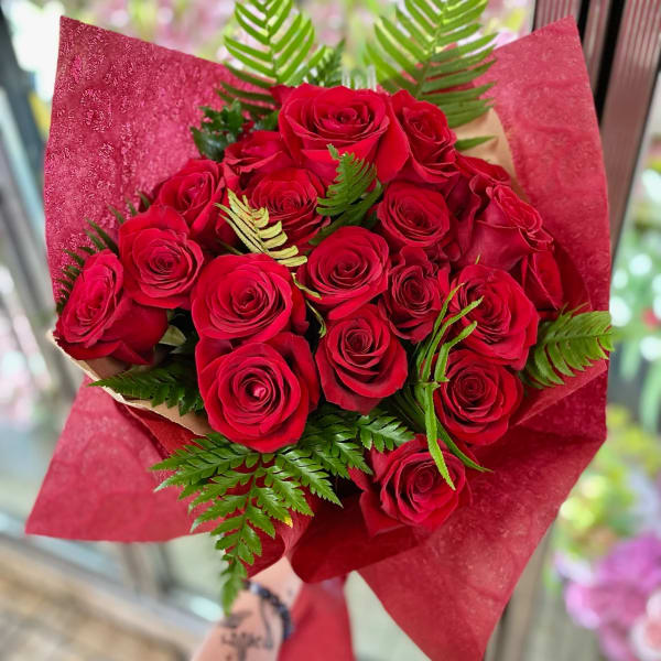 Bouquet of red roses wrapped in red paper with fern accents