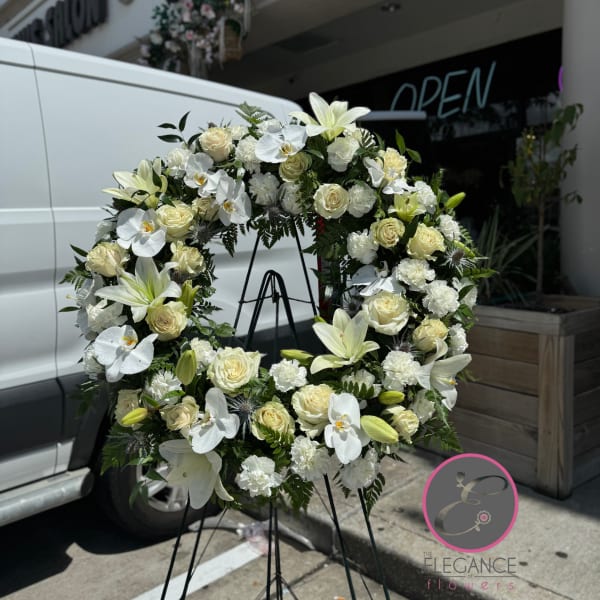 White floral wreath on a black stand with roses and lilies