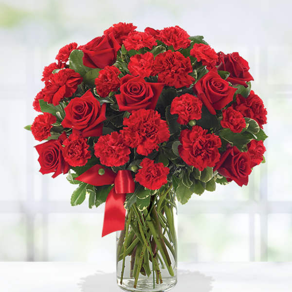 Red roses and carnations arranged in a clear glass vase with a red ribbon