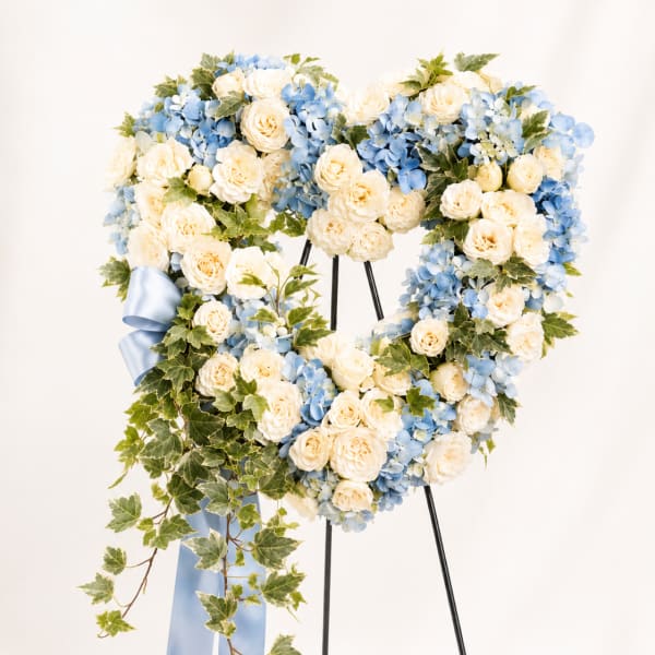 Heart-shaped floral wreath with cream roses and blue hydrangeas on a stand