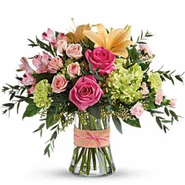 Mixed bouquet of pink roses, lilies, and green blooms in a clear glass vase with ribbon