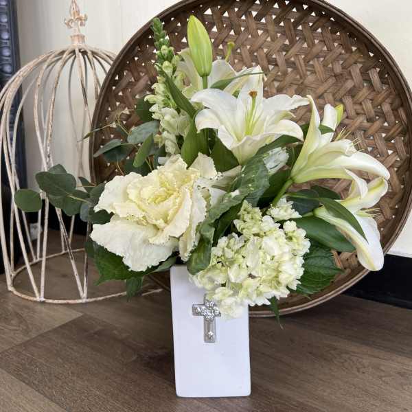White lilies and pale flowers in a white vase with a cross emblem