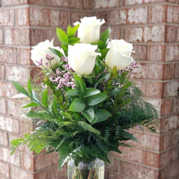 White roses arranged in a clear glass vase with greenery