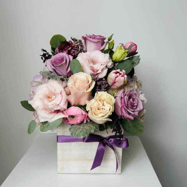 Pink and lavender roses arranged in a square box with a purple ribbon