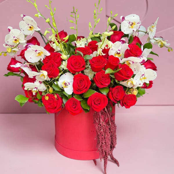 Red roses and white orchids arranged in a pink hat box