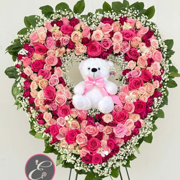 Heart-shaped pink rose arrangement with a white teddy bear in the center