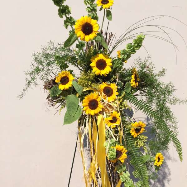 Tall sunflower arrangement with yellow ribbons and greenery on a stand
