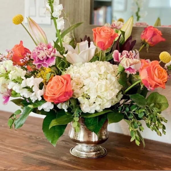 Mixed bouquet of coral roses, white hydrangea, and lilies in a silver vase