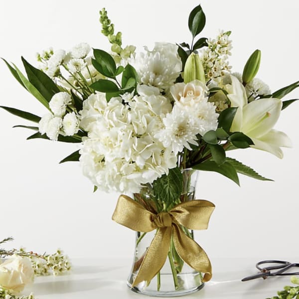 White floral bouquet in a clear glass vase with a gold ribbon
