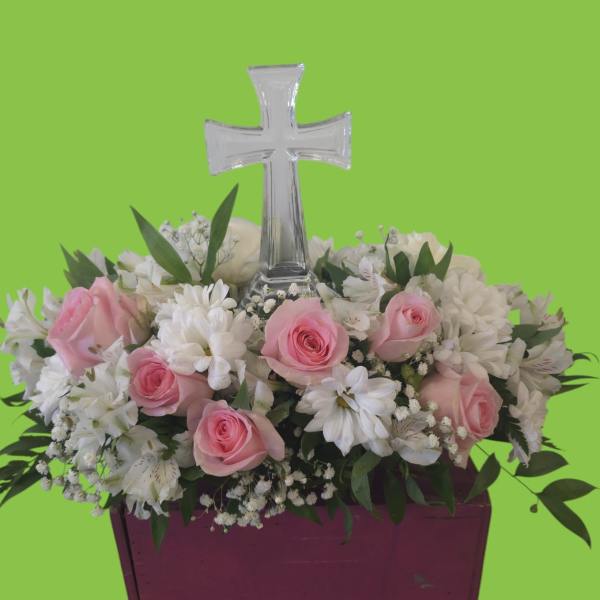 Pink roses and white flowers arranged around a clear cross in a purple container