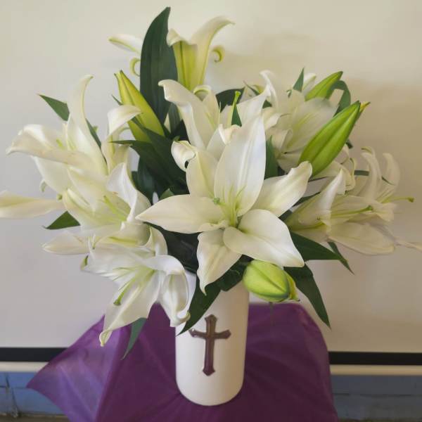 White lilies arranged in a white vase with a cross emblem