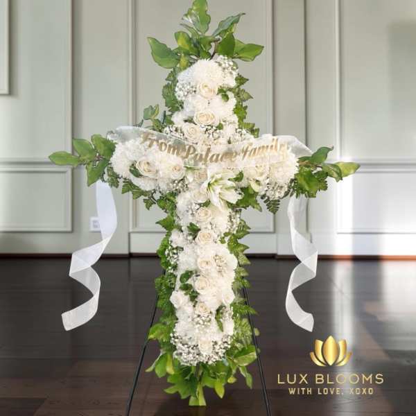 White floral cross arrangement with ribbon streamers and greenery