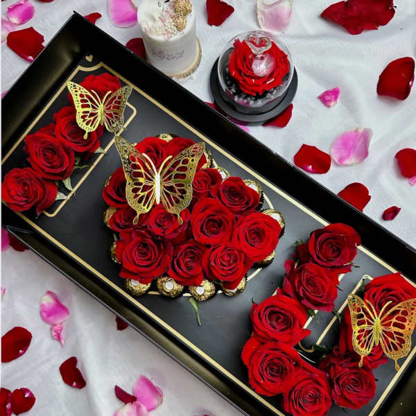 Red roses arranged in a black gift box with gold butterfly accents