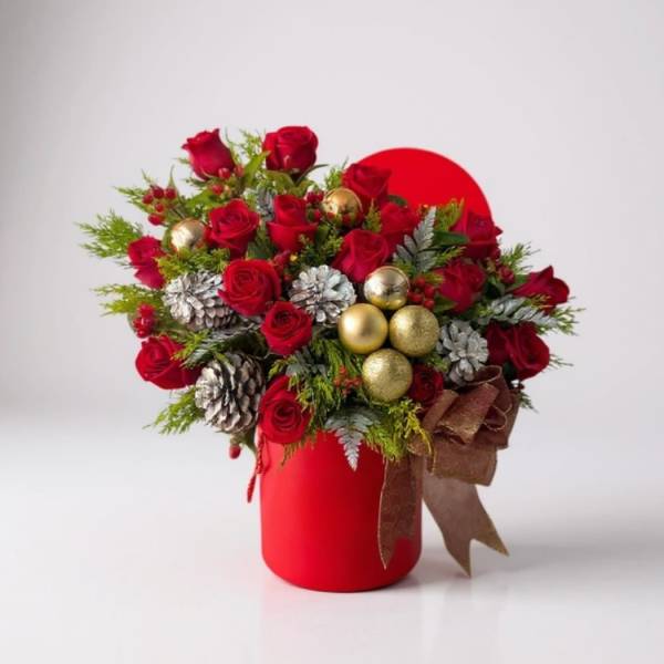 Red roses arranged in a red vase with gold ornaments and pinecones