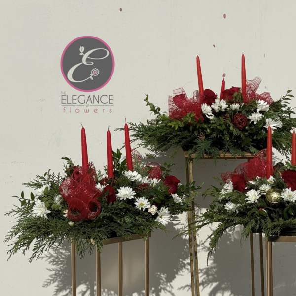 Three red-and-white floral arrangements with tall red candles on gold stands