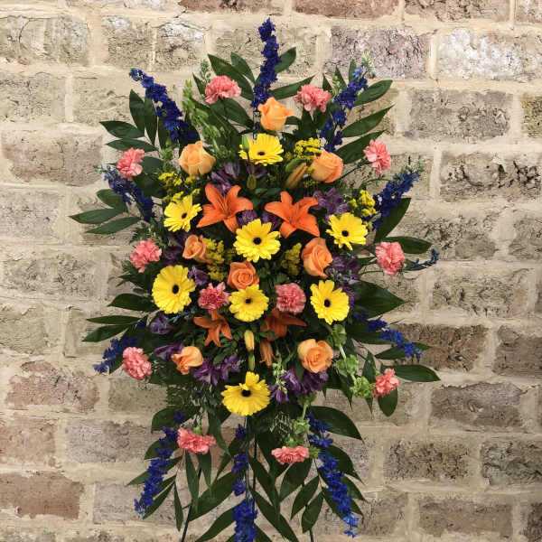 Standing floral spray with orange roses, yellow daisies, and blue accents