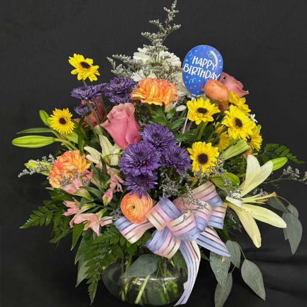 Mixed bouquet in a glass vase with a birthday pick and striped ribbon