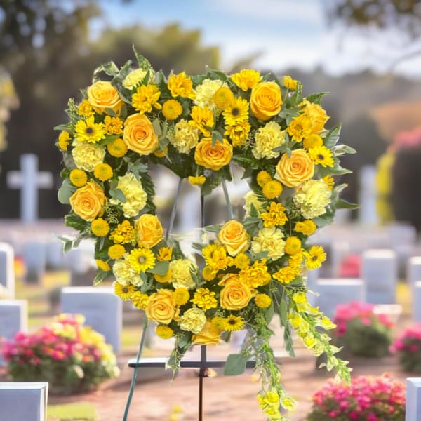 Yellow floral heart-shaped funeral wreath on a stand