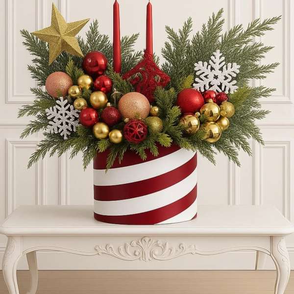 Christmas arrangement with red candles, ornaments, and evergreen branches in a striped container