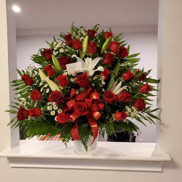 Large bouquet of red roses and white lilies in a white vase with a red ribbon