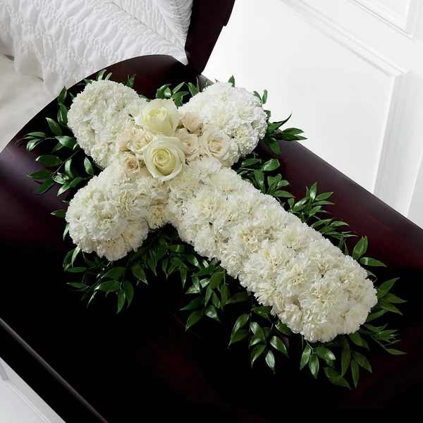 White floral cross arrangement on a dark casket