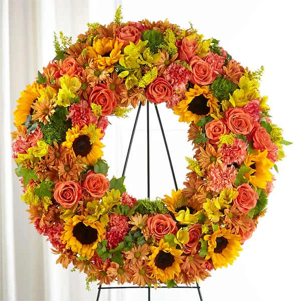 Large floral wreath with sunflowers, roses, and orange blooms on a black stand