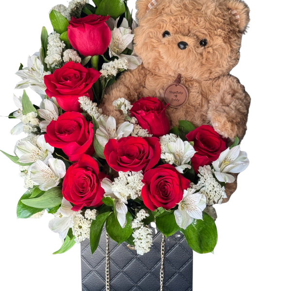 Red roses and white flowers arranged with a teddy bear in a quilted handbag box