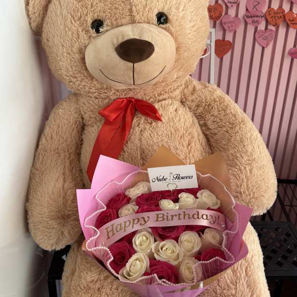 Large teddy bear holding a bouquet of pink and white roses
