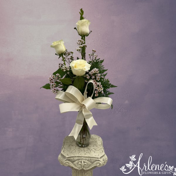 White roses in a glass vase with a cream ribbon bow