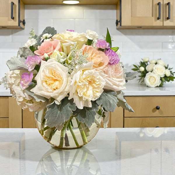 Bouquet of cream, blush, and lavender flowers in a clear glass vase