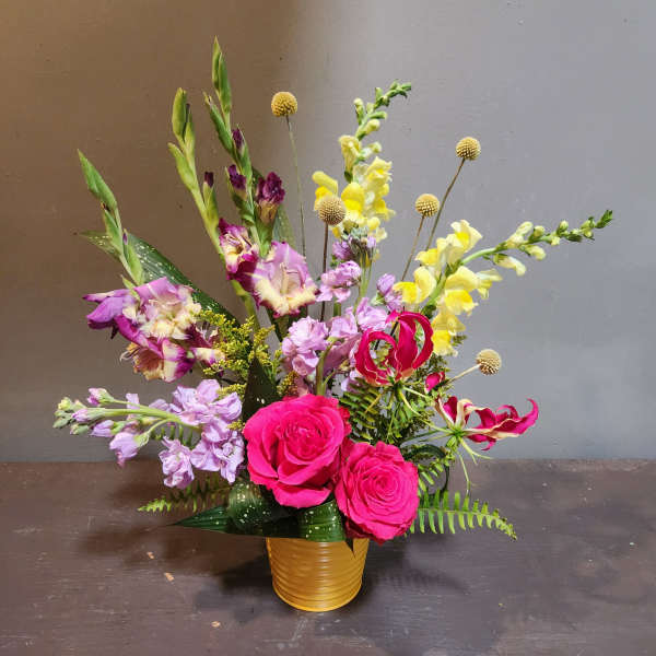 Bright mixed bouquet with pink roses and yellow snapdragons in a gold vase