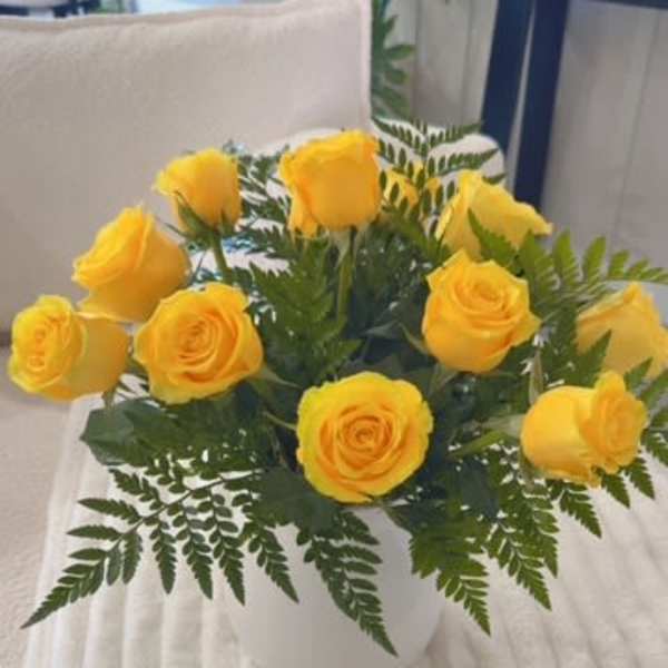 Yellow roses arranged in a white vase with fern foliage