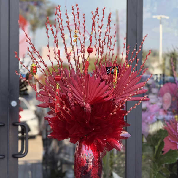 Tall red floral arrangement in a metallic vase with decorative hanging ornaments