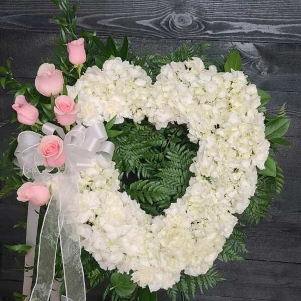Heart-shaped white floral wreath with pink roses and a white ribbon bow
