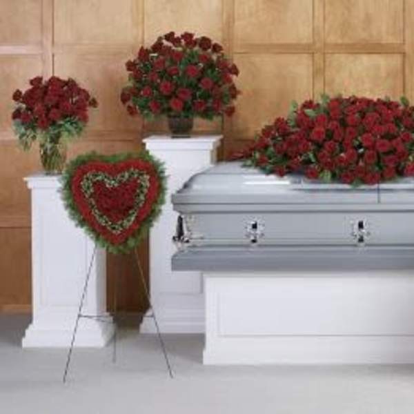 Funeral casket surrounded by red rose arrangements and a heart-shaped wreath with green border
