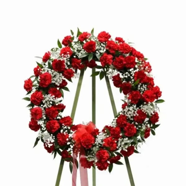 Red carnation funeral wreath with white filler flowers on a stand