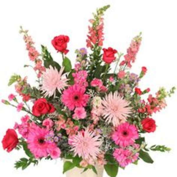 Pink and red mixed flower arrangement in a cream vase