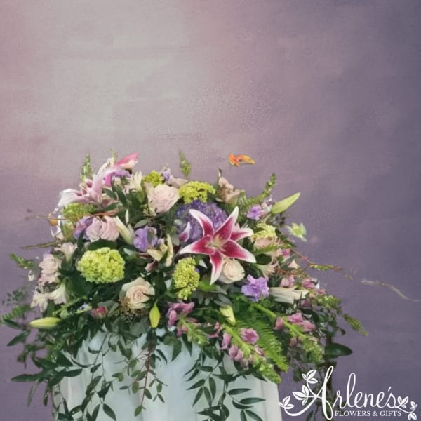 Large floral arrangement with pink lilies, roses, and purple blooms in a white container