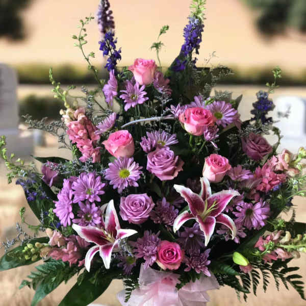 Pink and purple mixed flower arrangement in a white basket with ribbon