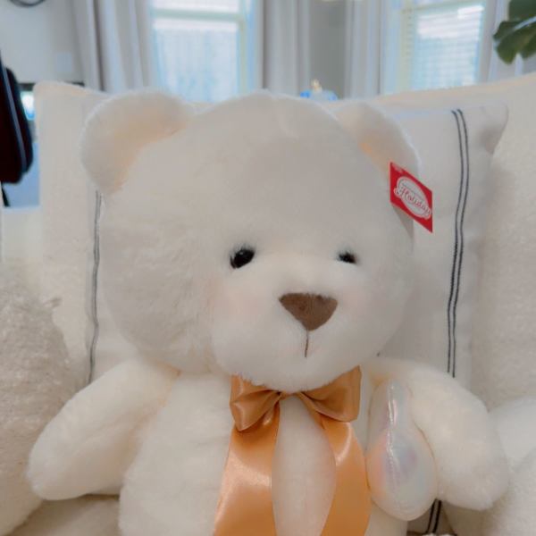 White teddy bear with an orange ribbon sitting on a couch