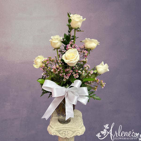 White roses in a glass vase with a white ribbon bow